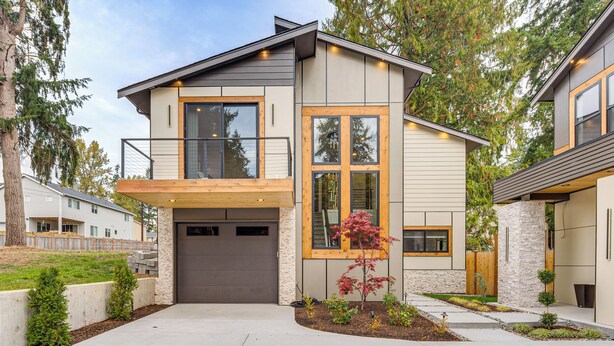 Une maison moderne à deux étages, dotée d’un garage, d’un balcon et d’un jardin paysager à l’avant.