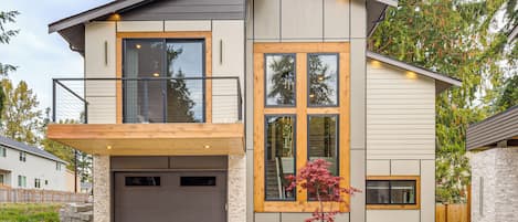 A modern two-story house with a garage, a balcony, and a stone exterior.