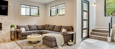 A modern living room with a sectional sofa, a coffee table, and a staircase leading to an upper floor.