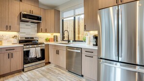 Une cuisine moderne dotée d’appareils électroménagers en acier inoxydable, de meubles en bois et d’un revêtement mural en carreaux.