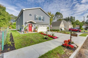 A two-story house with a red front door, a garage, and a well-maintained lawn with colorful flower beds.