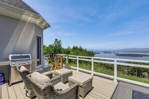 A deck with outdoor furniture, a grill, and a view of a lake and forest.