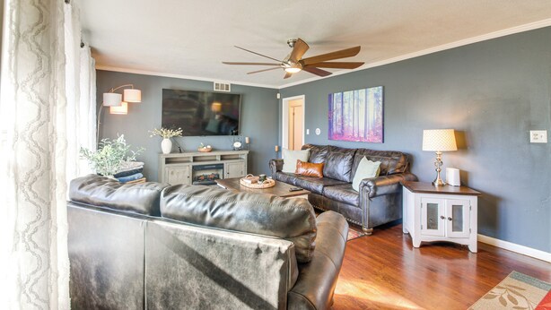A living room with a sofa set, a television, a ceiling fan, and a small cabinet. - Easy OKC Access! Quiet Home w/ Yard & Workspace (Midwest City)