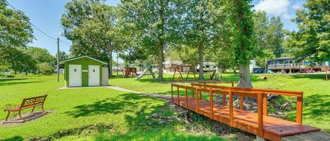 Un parque con un puente de madera, un cobertizo pequeño y un parque infantil.