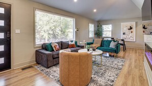A spacious living room with a large window, a sofa, a coffee table, and a green armchair. - Close to Decatur Square: Family Home w/ Deck! (Decatur)