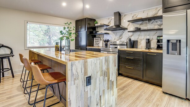 A modern kitchen with a marble backsplash, stainless steel appliances, and a central island with bar stools. - Close to Decatur Square: Family Home w/ Deck! (Decatur)