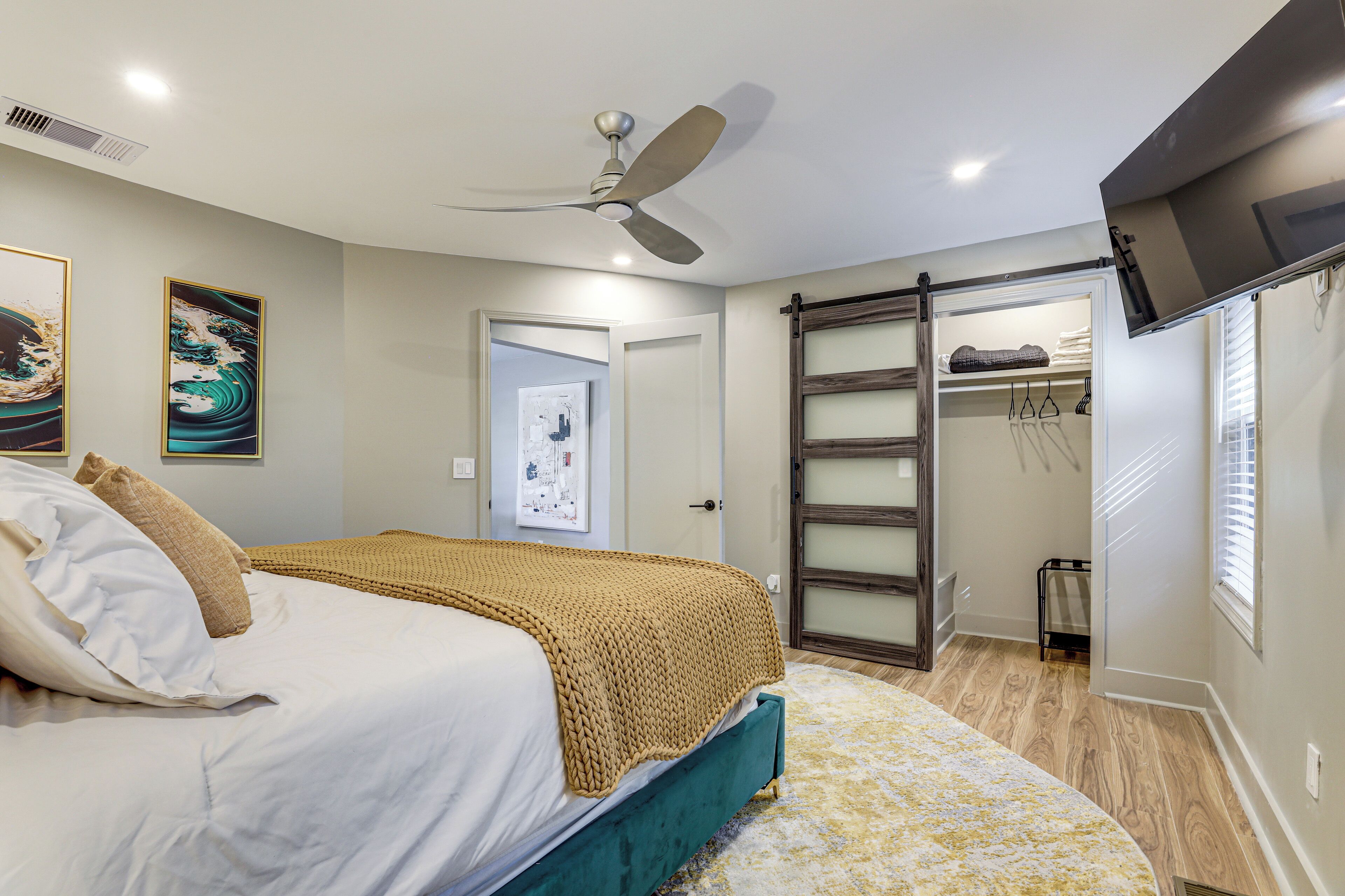 A bedroom with a bed, a ceiling fan, a wardrobe, and a door leading to another room.