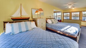 Een slaapkamer met twee bedden, een houten hoofdbord, een dressoir, een spiegel en een model zeilboot.