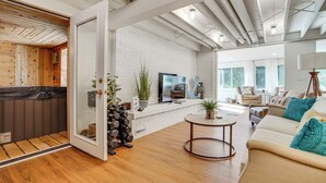 A modern living room with a white brick wall, wooden flooring, a sofa, a coffee table, and a TV. - Cabin w/ Halstead Bay Access: Hot Tub, Sauna, Dock (Mound)