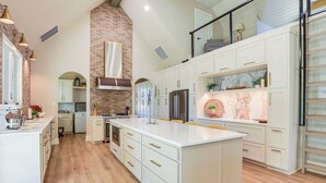 A spacious kitchen with a large island, white cabinetry, and a brick accent wall. - Walk to Shops & Winery! Stylish Dtwn Ovilla Home (Red Oak)