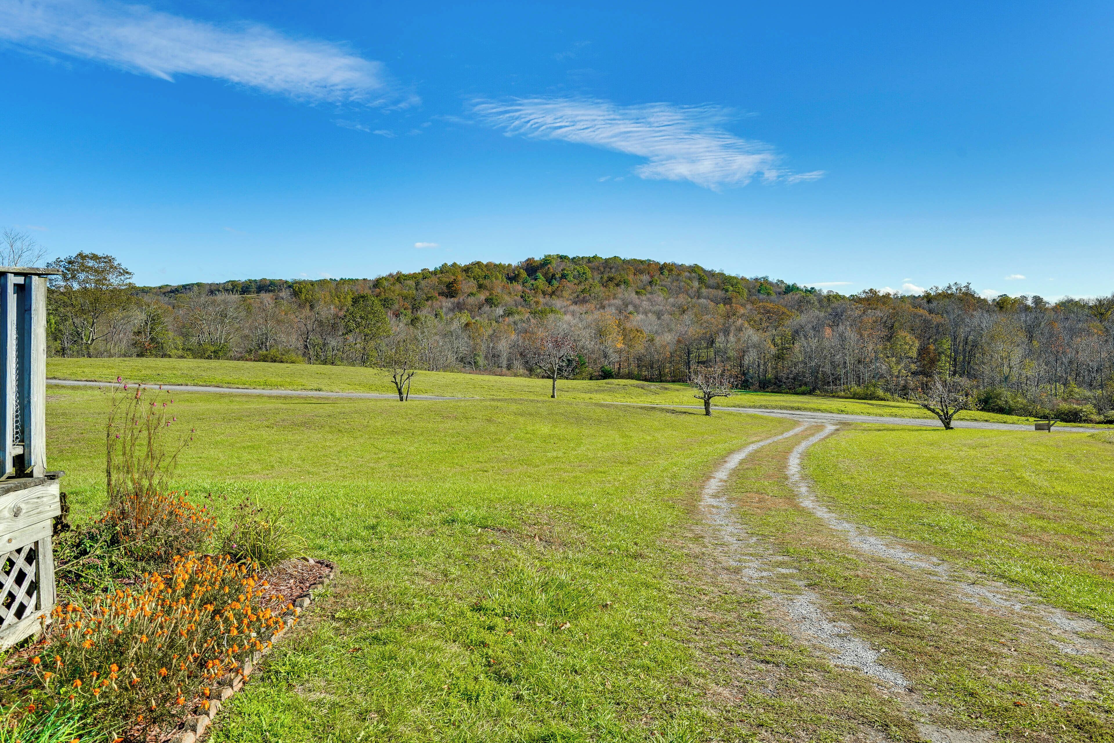 A grassy field with a dirt path leading to a building with a wooden fence and a bench.