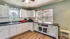 A kitchen with white cabinets, a wooden floor, a ceiling fan, and a window with blinds. - Walk to Restaurant & Bar: Home w/ Deck in Gary (Gary)