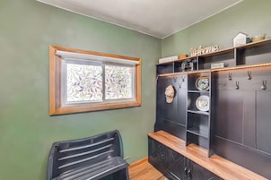 Una habitación con ventana, una silla negra, un banco de madera y un mueble negro con estantes.