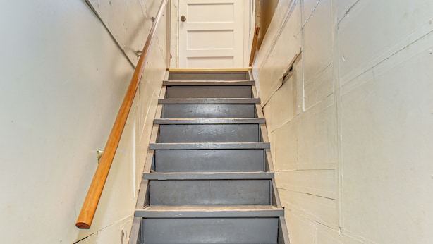 Eine enge Treppe mit hölzernen Geländern und einer weißen Tür oben.
