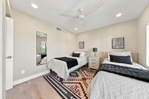 A bedroom with two beds, a ceiling fan, a bedside table with a lamp, a mirror, and a rug.