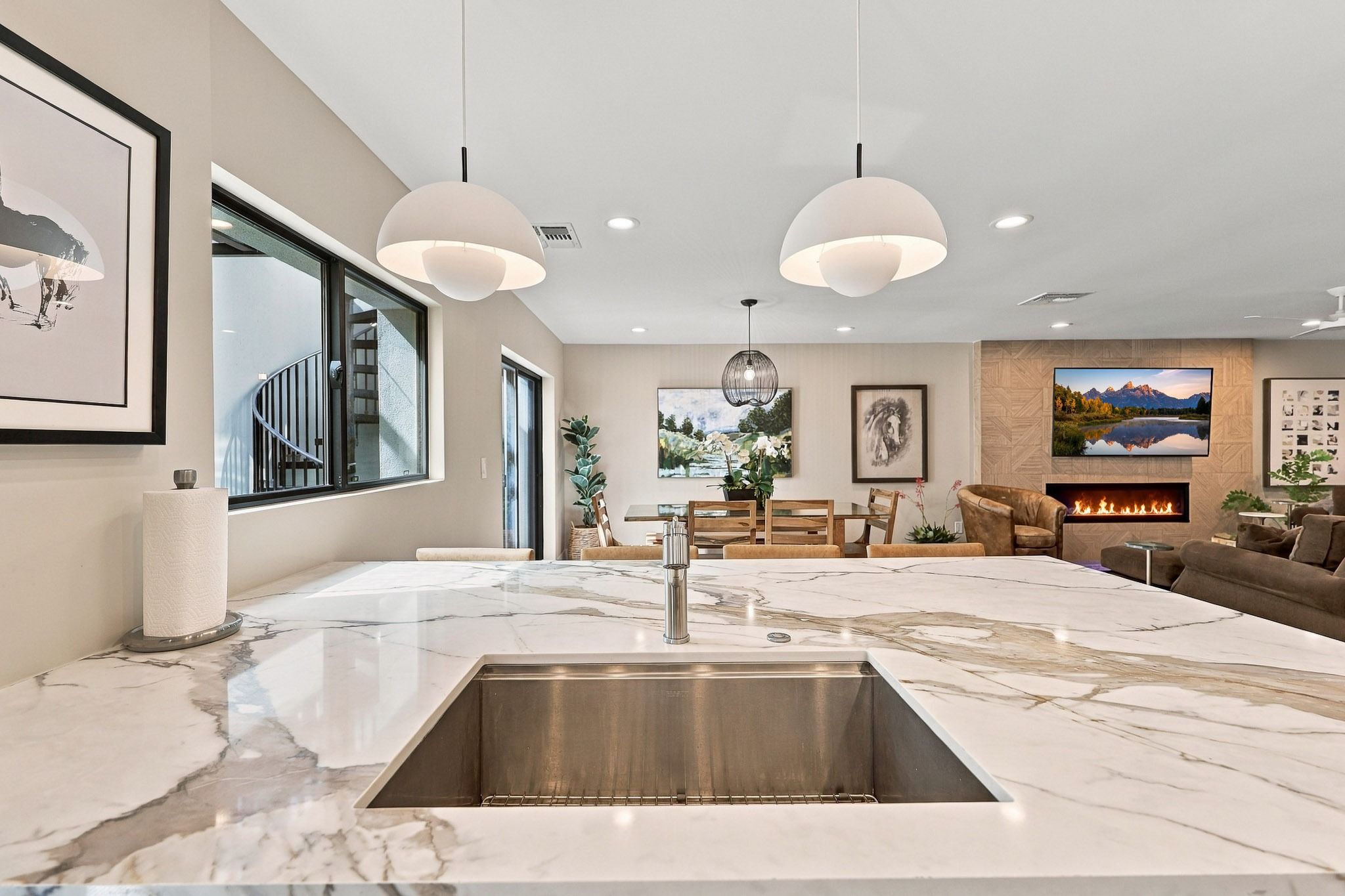 A modern kitchen with a marble countertop, stainless steel sink, and pendant lighting.
