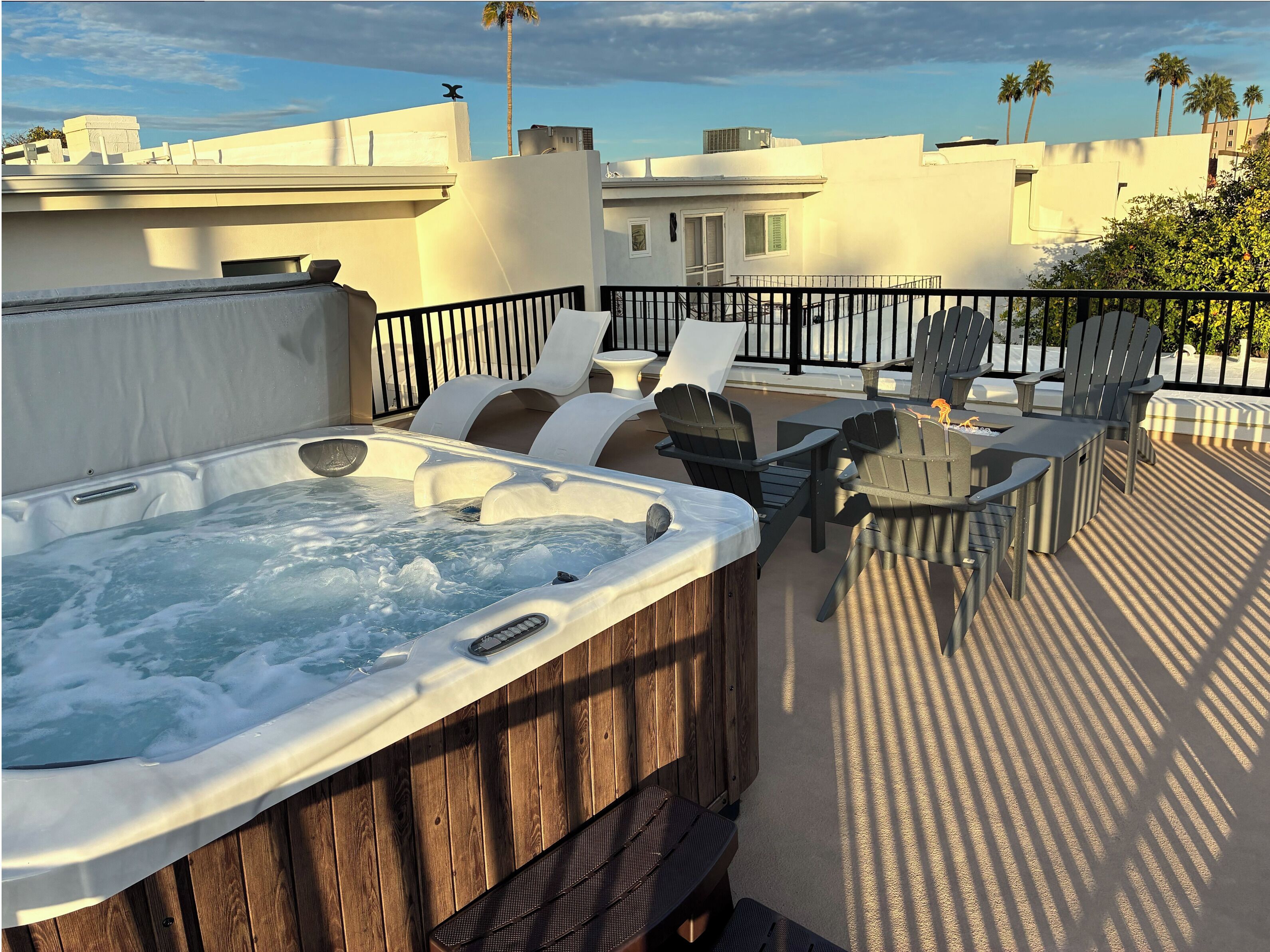 A hot tub on a rooftop patio with outdoor furniture and a view of the cityscape.