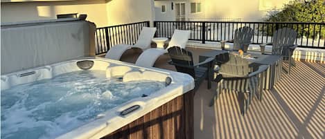 A hot tub on a rooftop patio with outdoor furniture and a view of the cityscape.