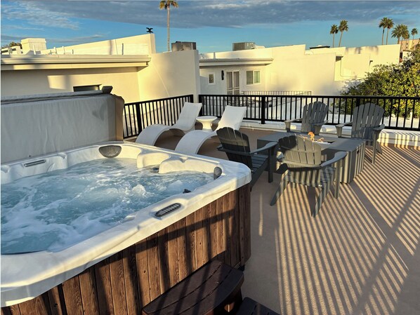 A hot tub on a rooftop patio with outdoor furniture and a view of the cityscape.