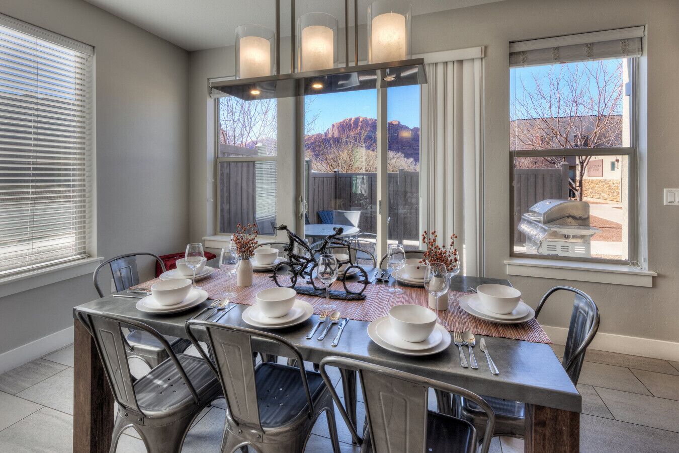 A dining area with a table set for six, chairs, a bicycle, and a view of mountains through large windows.