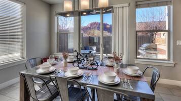 A dining area with a table set for six, chairs, a bicycle, and a view of mountains through large windows.