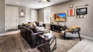 A living room with a sofa, coffee table, armchair, TV, and a ceiling fan.