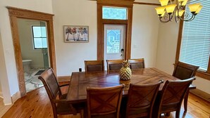 A dining room with a wooden table, six chairs, a chandelier, and a door with a window.