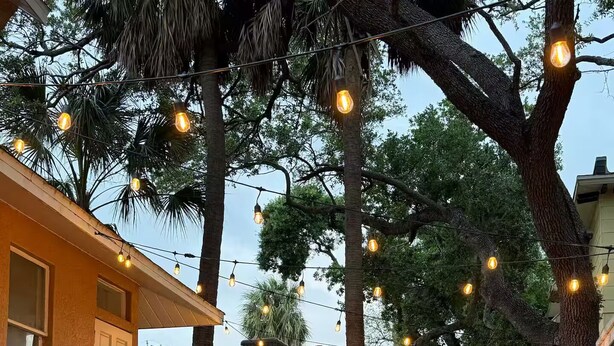 An outdoor patio with a brick floor, metal railing, and string lights.
