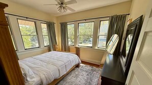A bedroom with a bed, a ceiling fan, a dresser, and large windows.