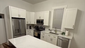 A modern kitchen with white cabinetry, a central island with bar stools, stainless appliances, and a pendant light.