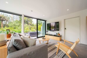 A modern living room with a sofa, a coffee table, a TV, and a view of greenery outside. - DUM Residences (Mexico City)