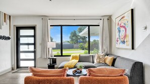 Un salon moderne avec un canapé gris, des fauteuils orange et une grande fenêtre donnant sur l’extérieur.