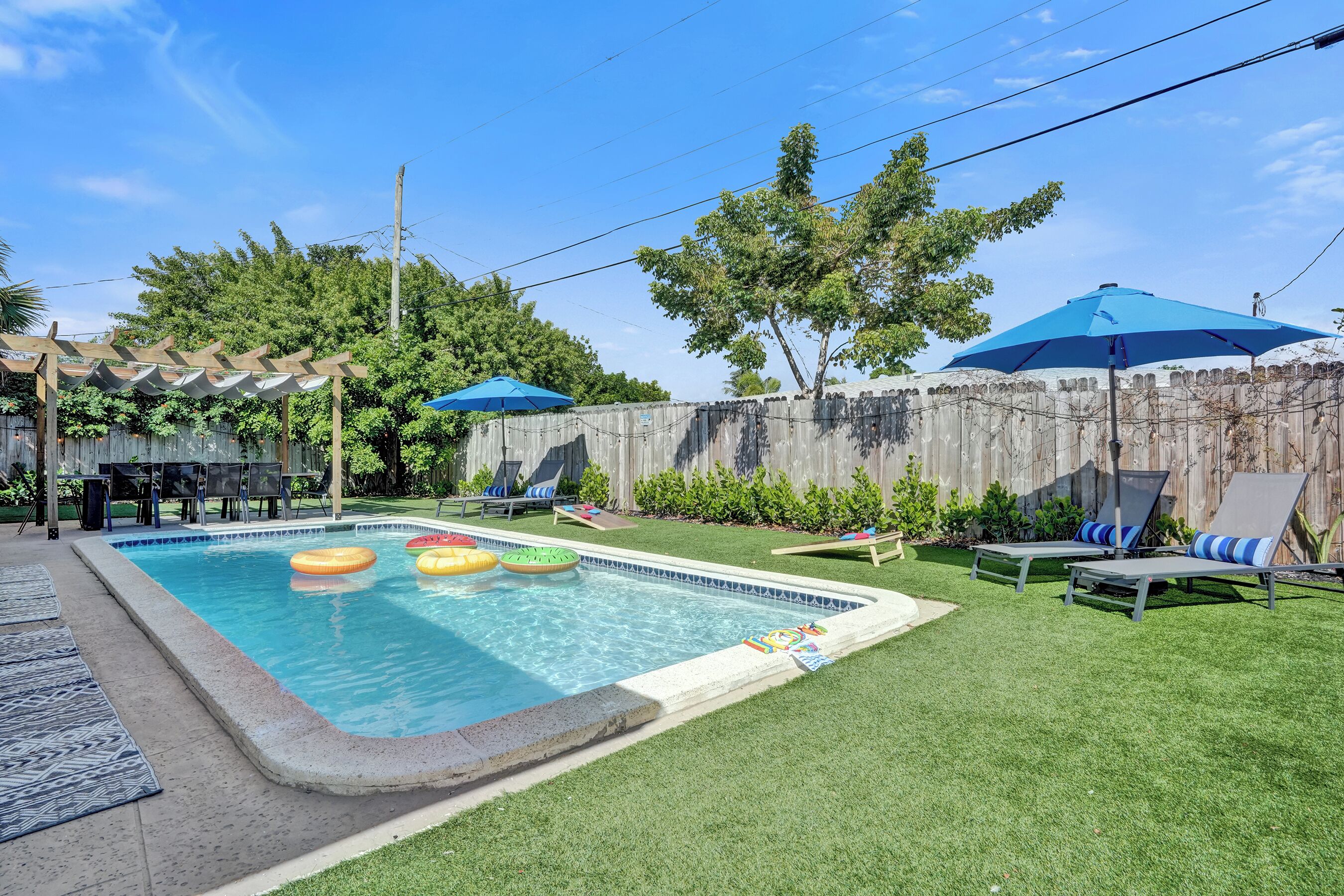 Un patio trasero con piscina, flotadores, sillas de descanso y una pérgola.