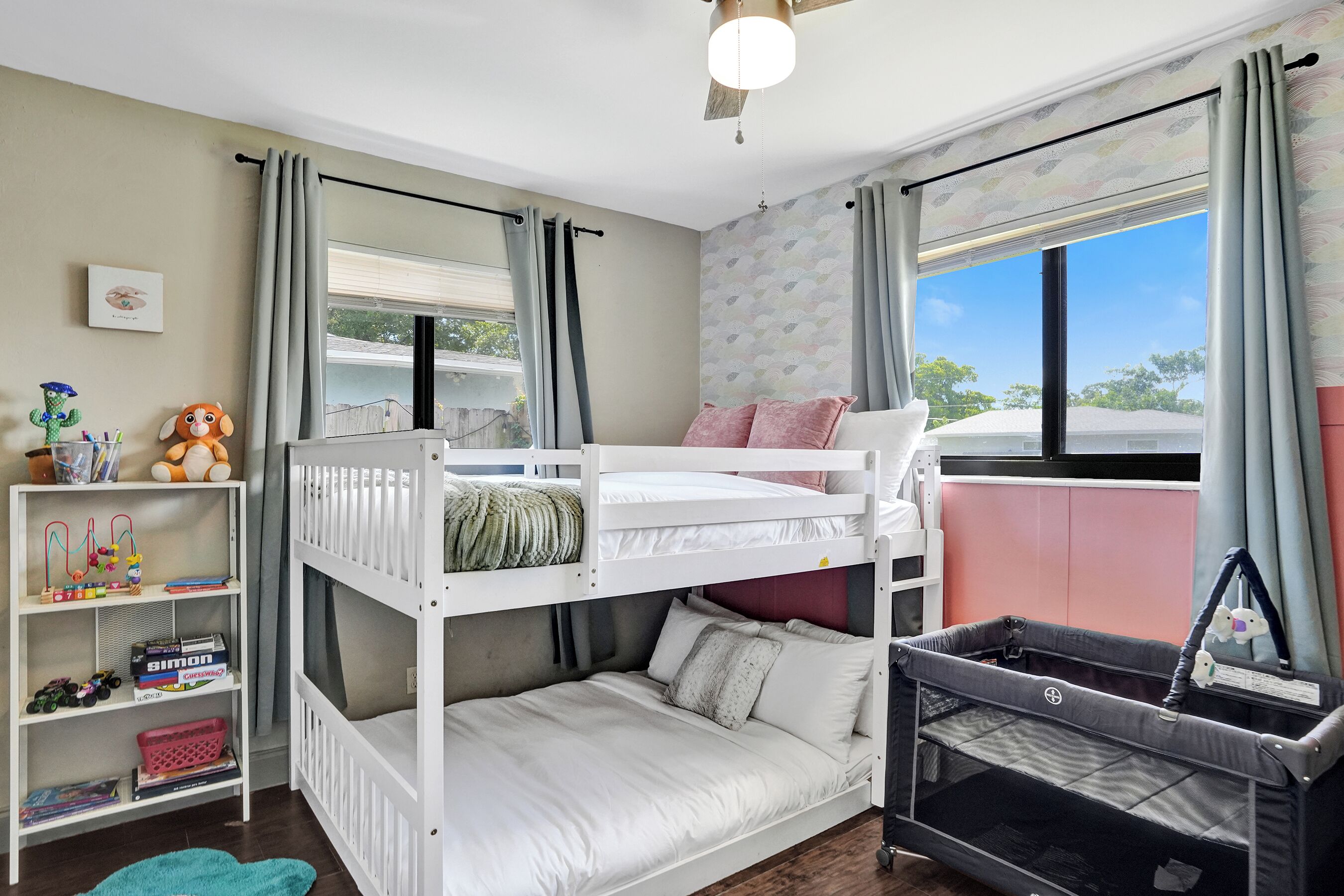 Een kinderkamer met stapelbedden, een ledikant, een boekenplank en een raam met gordijnen.
