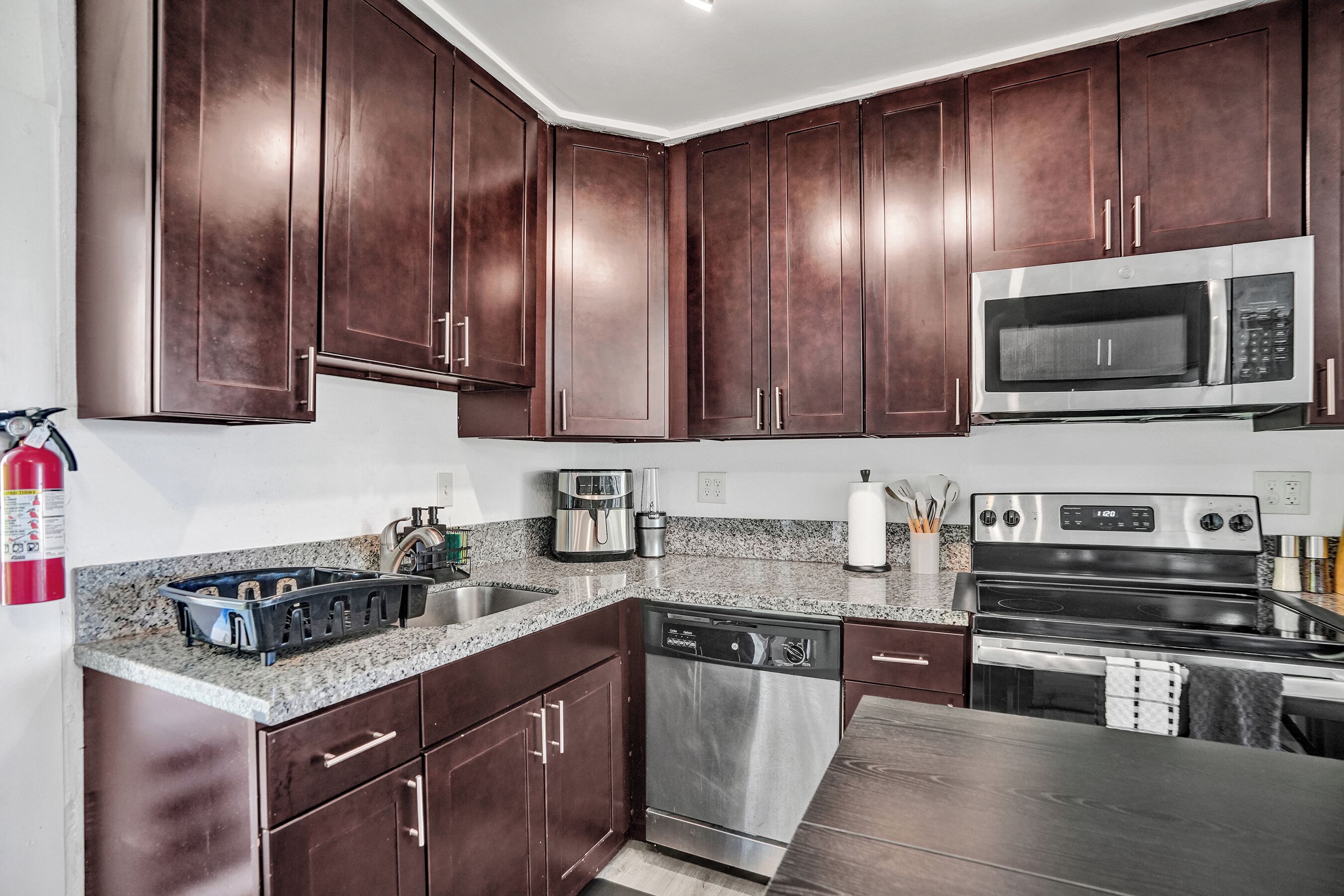 A kitchen with dark wooden cabinets, stainless steel appliances, granite countertops, and a dishwasher.