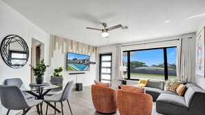 Un salon moderne comprenant un coin repas, un ventilateur de plafond, une grande fenêtre offrant une belle vue et un téléviseur fixé au mur.