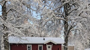 Una casa cubierta de nieve con fachada roja, puerta blanca y un pequeño porche.