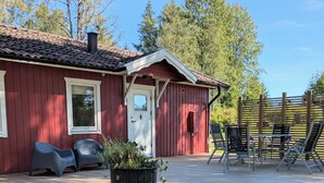 Una cabaña roja de madera con un balcón, asientos exteriores y una planta en maceta.