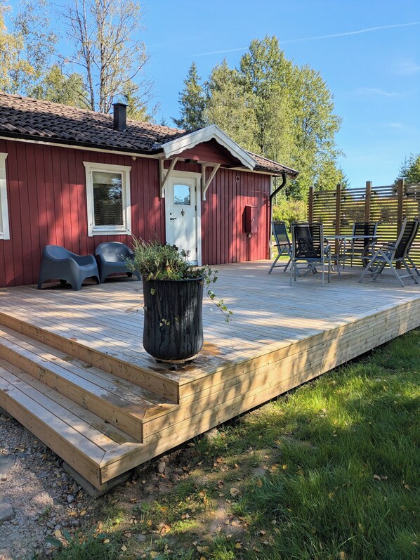 A red wooden cabin with a deck, outdoor seating, and a potted plant.