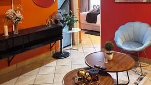 A modern living room with a red accent wall, a flat-screen TV, a round coffee table with decorative items, a blue chair, and a sofa with a heart-shaped cushion. - Enchanting 2-bedroom apartment in Nelspruit (Nelspruit)