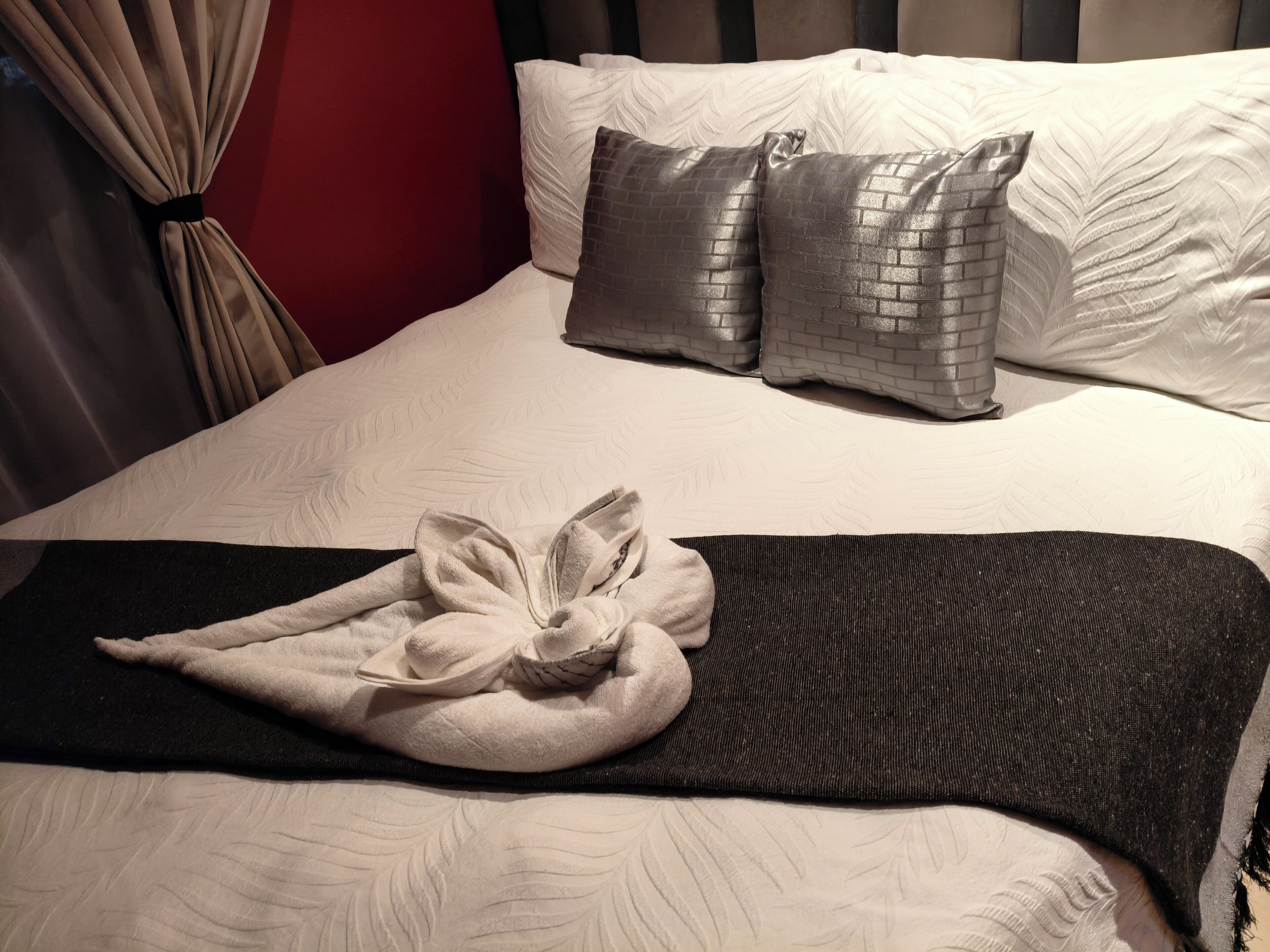 A neatly made bed with a white comforter, two grey pillows, and a black throw blanket.