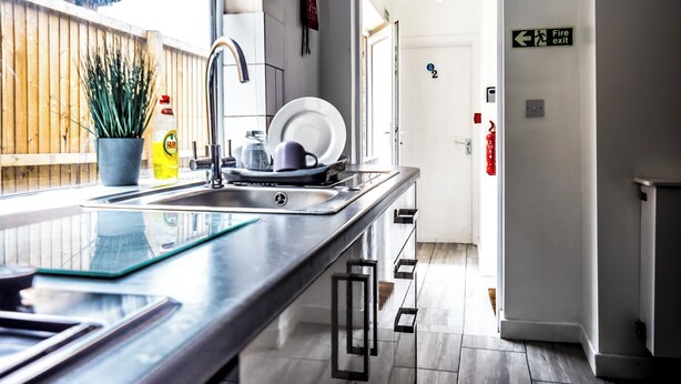 A modern kitchen with a stainless steel sink, a potted plant, and a fire exit sign.