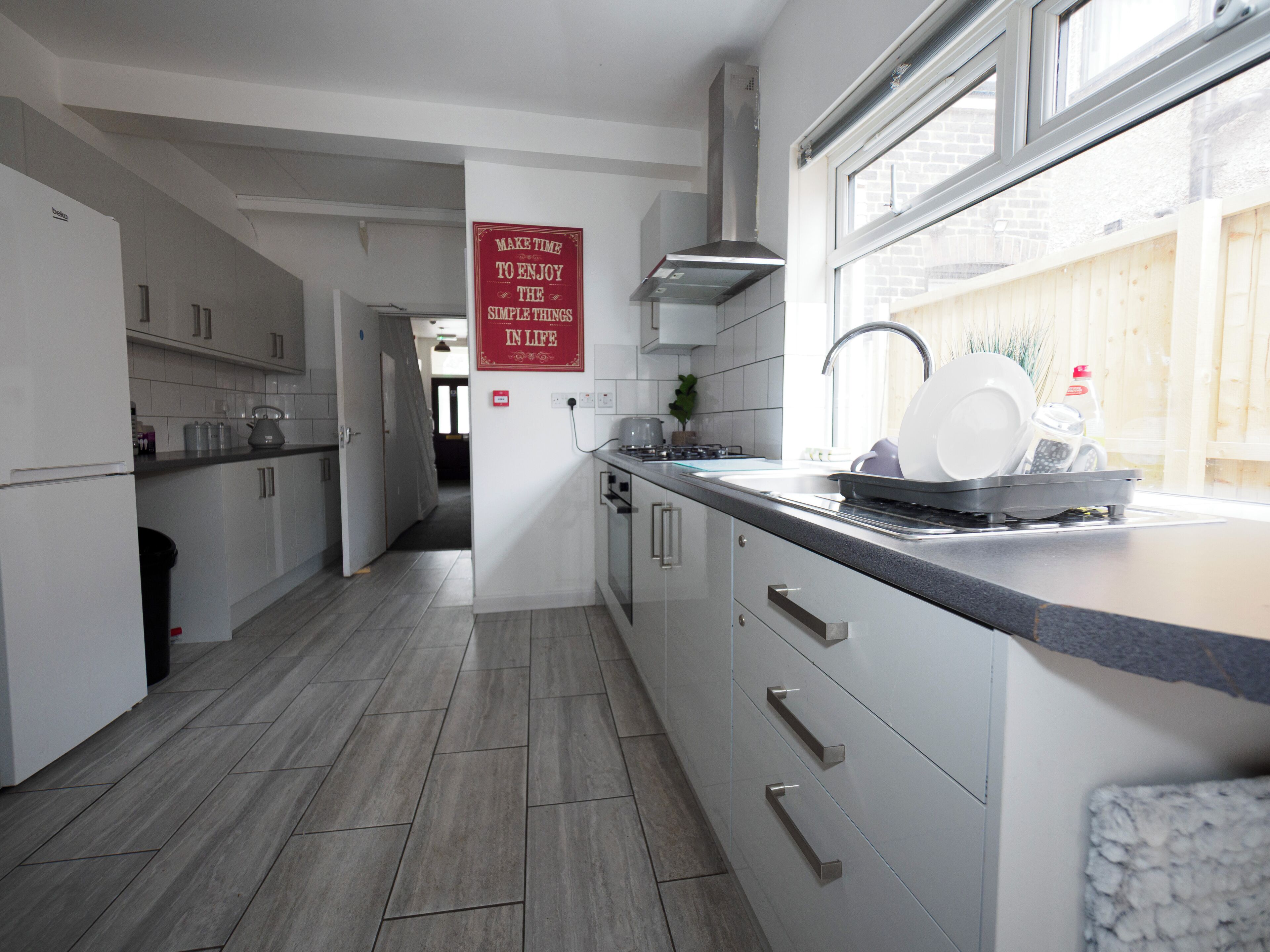 A modern kitchen with white cabinets, a stainless steel range hood, and a window with a view of a wooden fence.