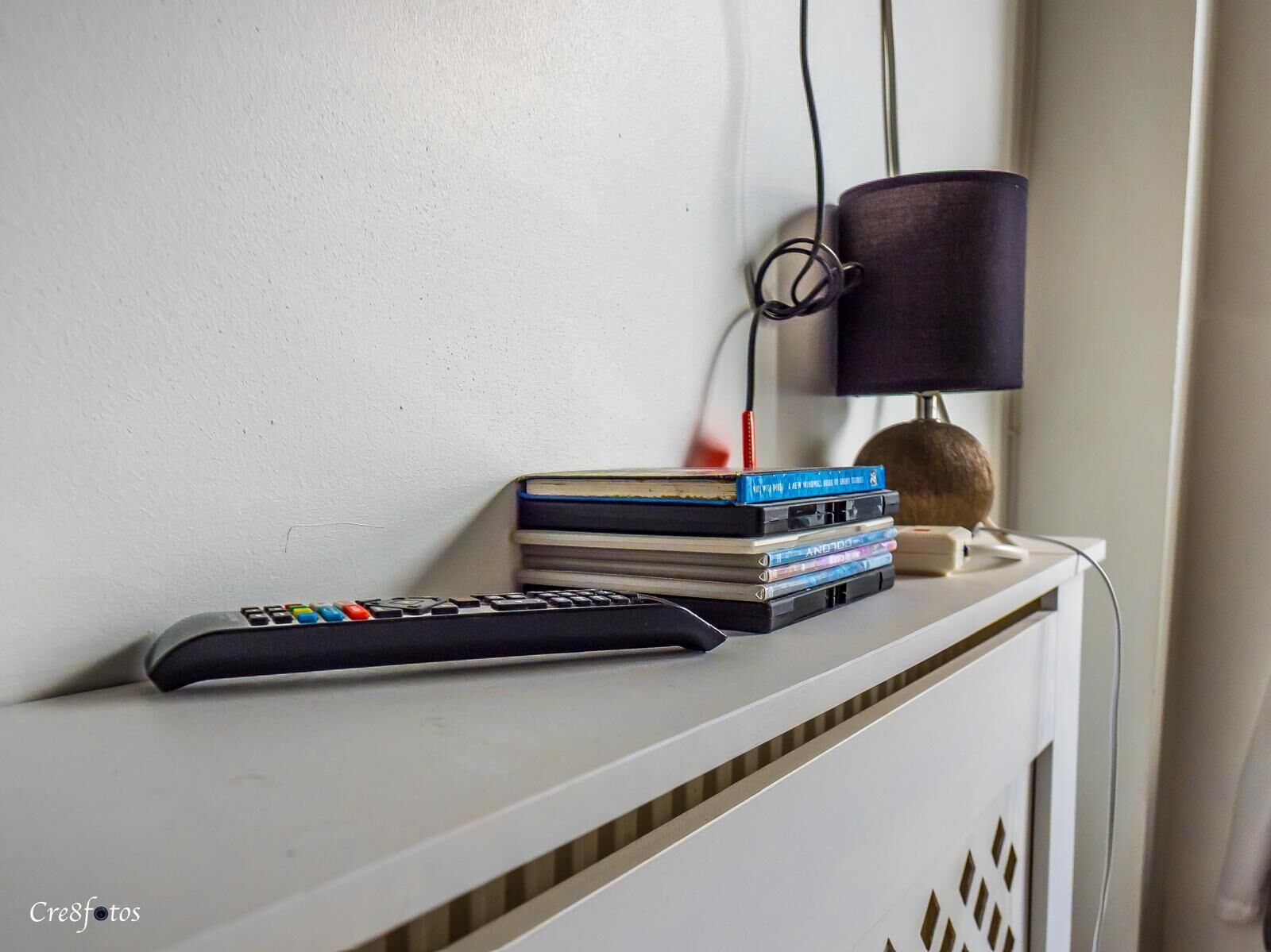 Een afstandsbediening, een stapel boeken en een lamp op een witte ondergrond.