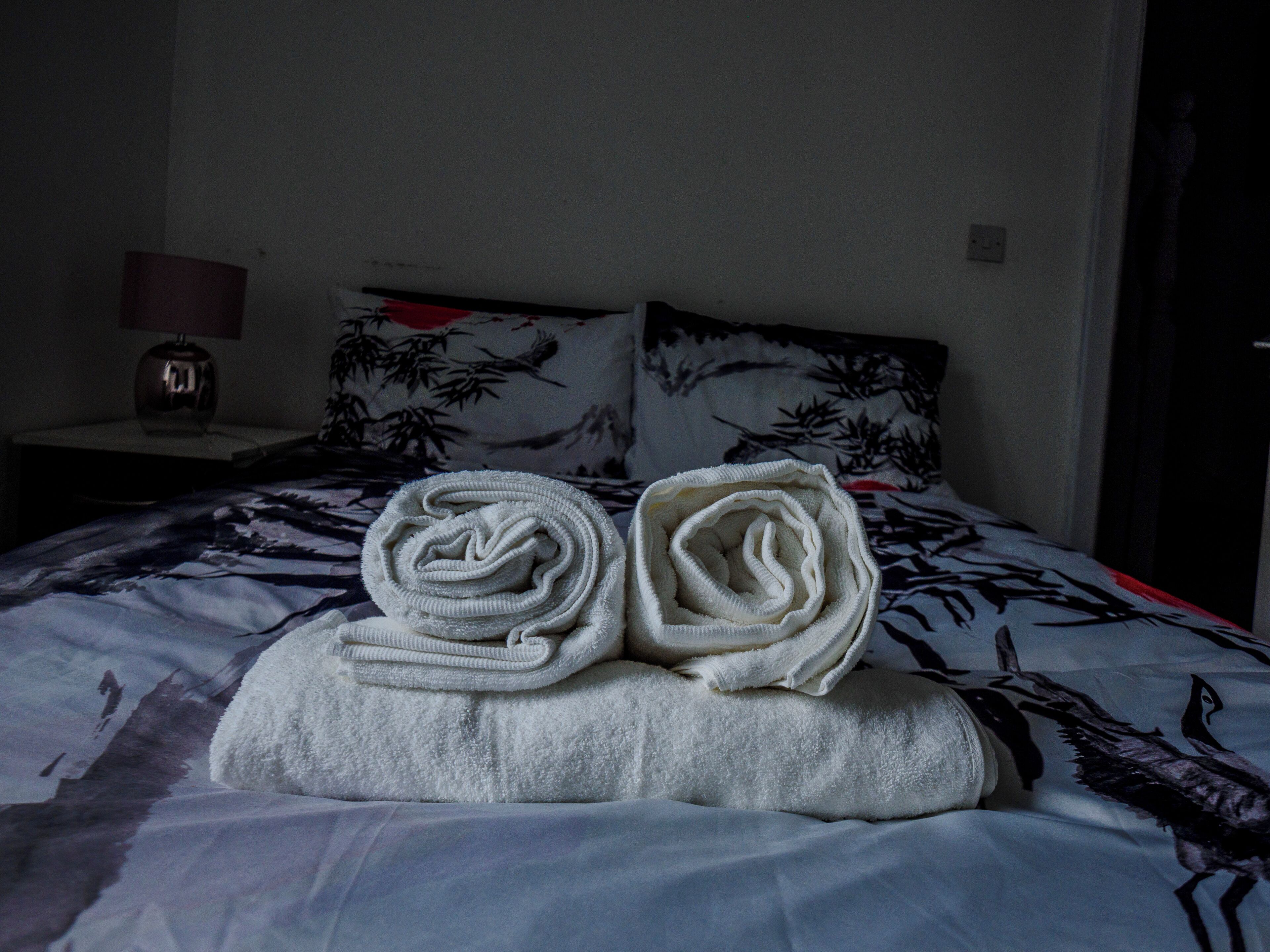 Ein ordentlich gemachtes Bett mit zwei zusammengerollten Handtüchern auf einem Kopfkissen.