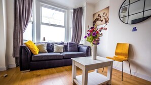 A modern living room with a grey sofa, a white coffee table, and a yellow chair. There is a vase with flowers on the coffee table.