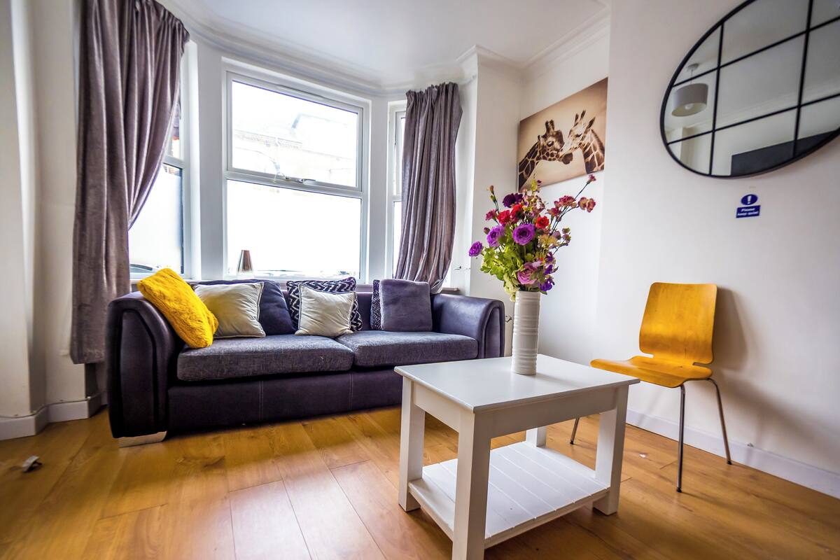 Un salon moderne avec un canapé gris, une table basse blanche et un fauteuil jaune. Un vase rempli de fleurs est posé sur la table basse.