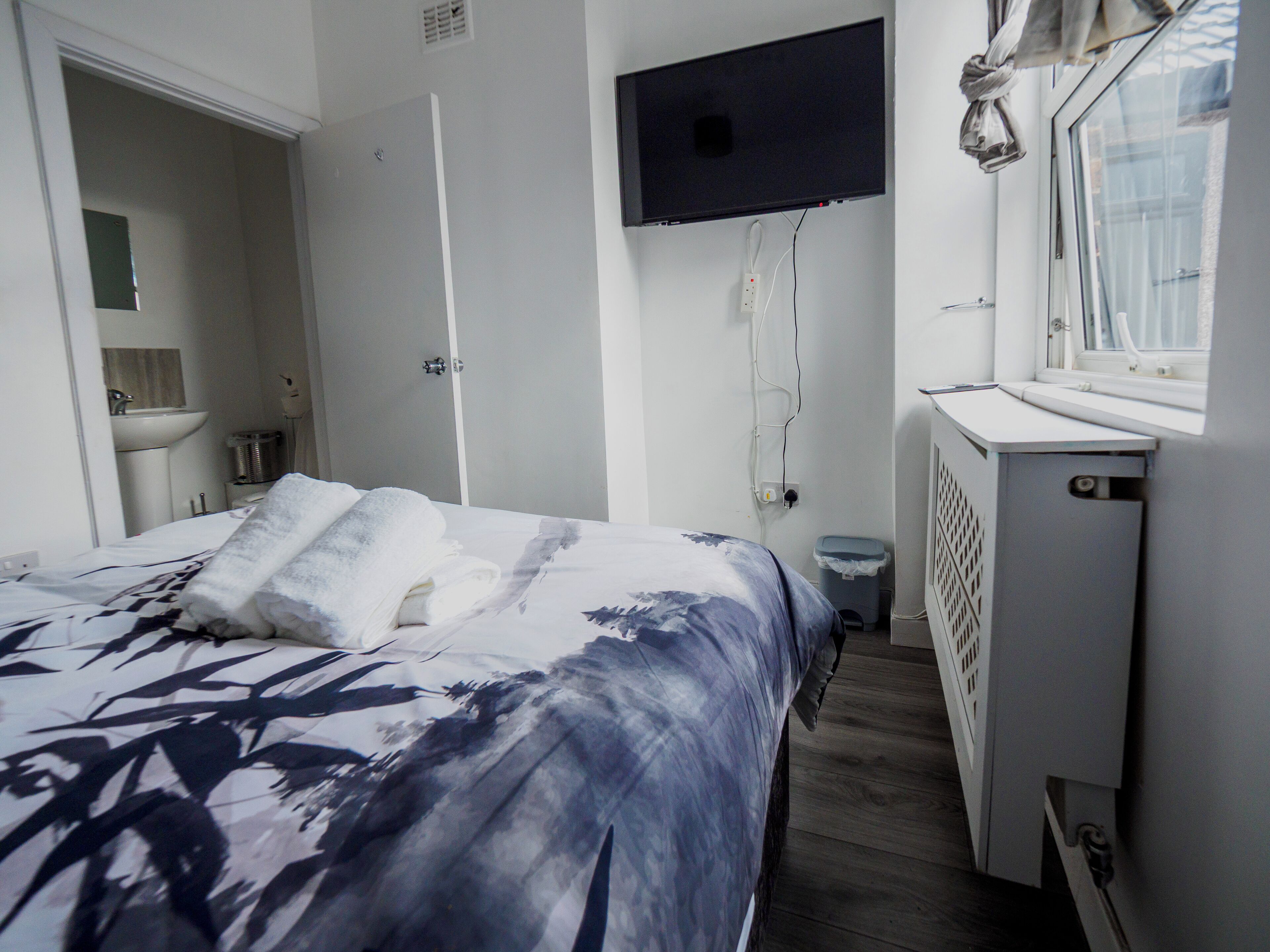 A bedroom with a bed, a TV mounted on the wall, a window, and a radiator.