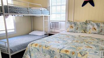 Una habitación con literas, una cama grande con colcha estampada, una ventana con persianas, un equipo de aire acondicionado y una decoración con forma de estrella de mar en la pared.