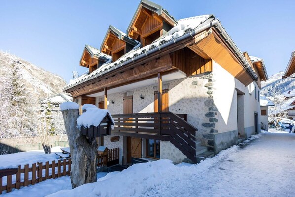 A chalet-style building with a wooden facade, stone accents, and a wooden staircase leading to the entrance.